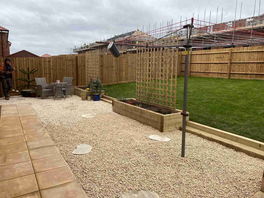 Low-maintenance gravel garden with sleeper planters, stepping stones and lawn