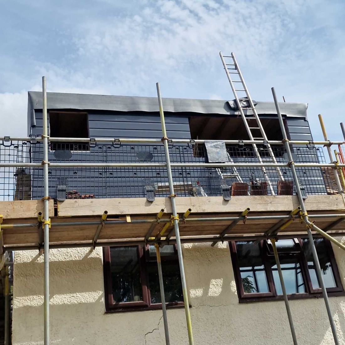 Rear dormer clad in dark grey with window openings ready, seen from the scaffold in Little Haywood