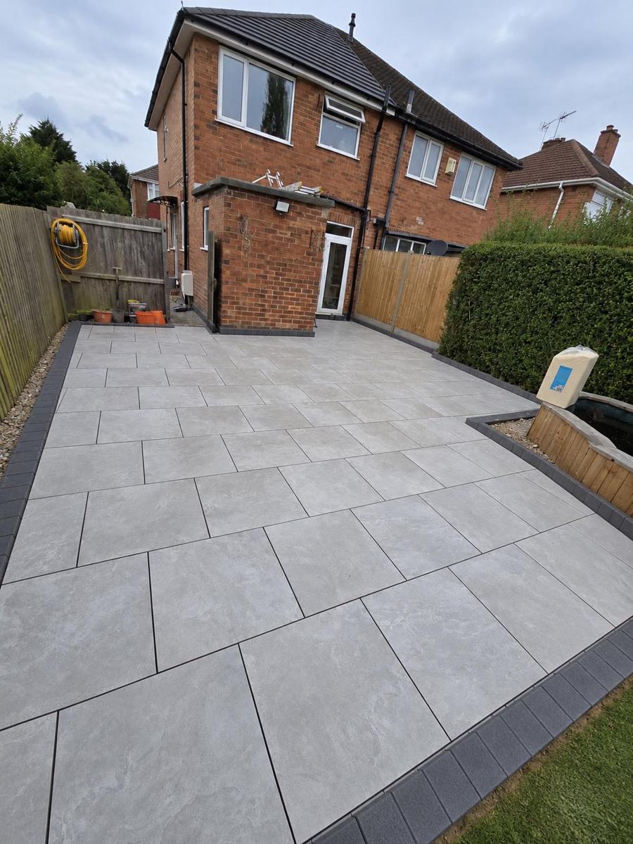New grey porcelain patio across the back garden of a semi-detached house, with a dark grey block border and a raised timber planter