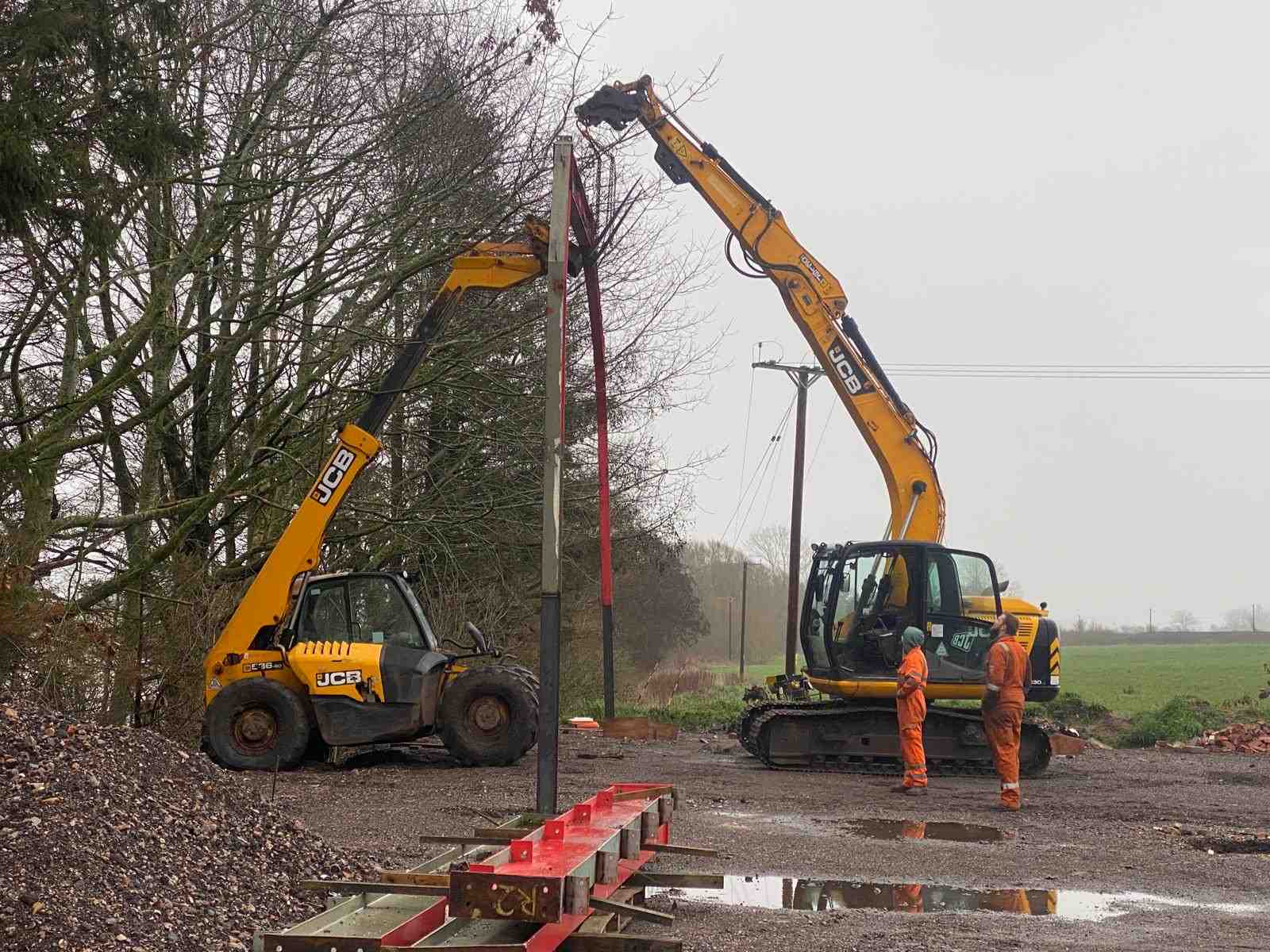 A JCB excavator and telehandler lifting a steel portal frame into place on a farm near Penkridge